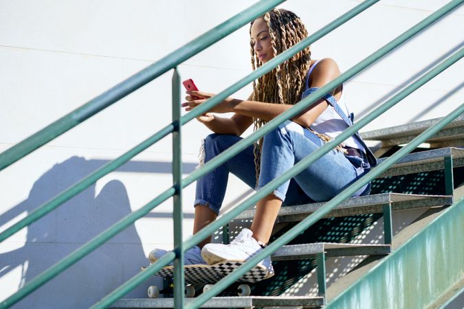 Serious female skater texting on phone on stairs, copy space