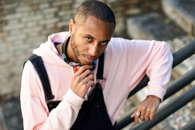 Pensive male in overalls and hoodie leaning on railing of stairs outside