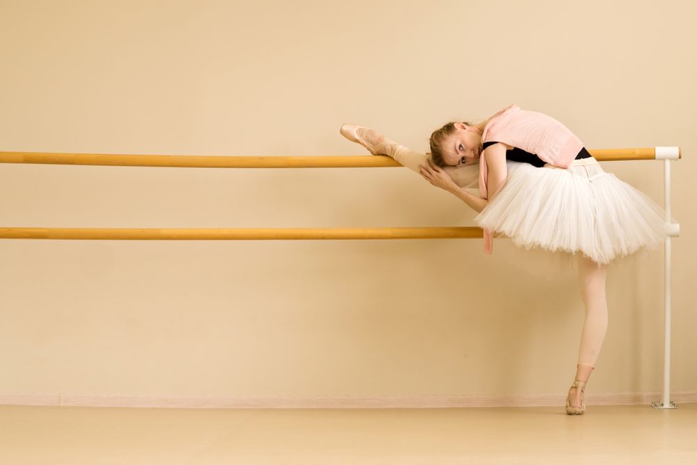 Ballerina holds intense stretch by leaning on barre