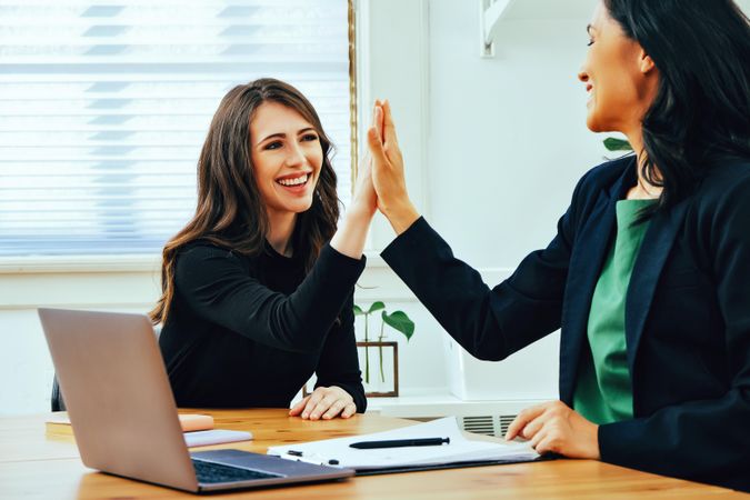 Two women doing a high five in bright office