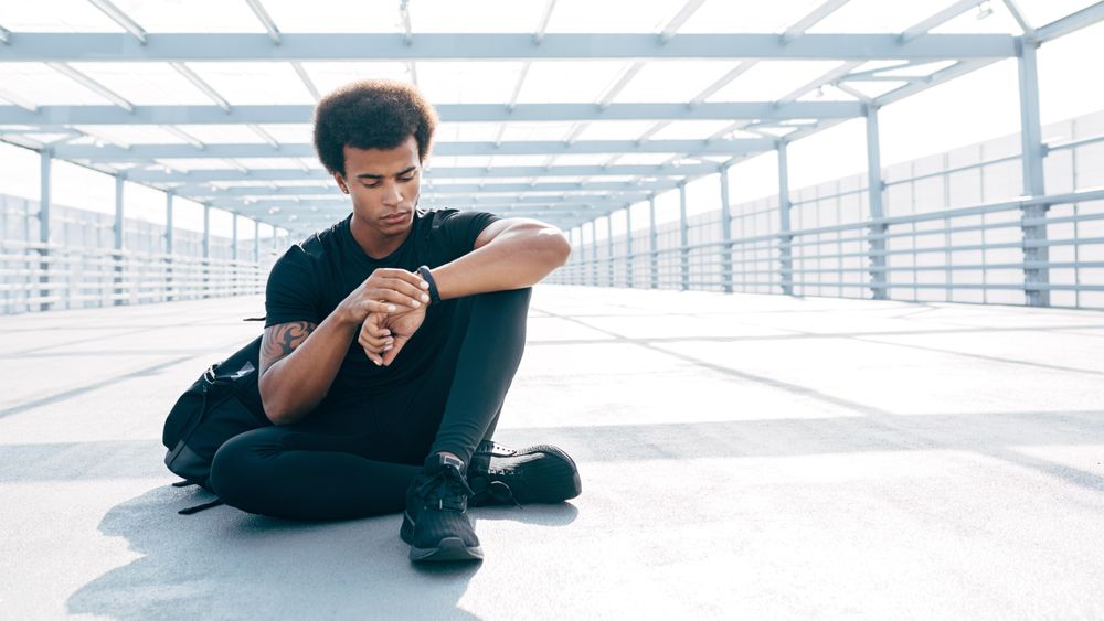 Male athlete resting and checking watch after training