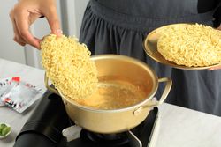 Chef putting circle of dried noodles into boiling water