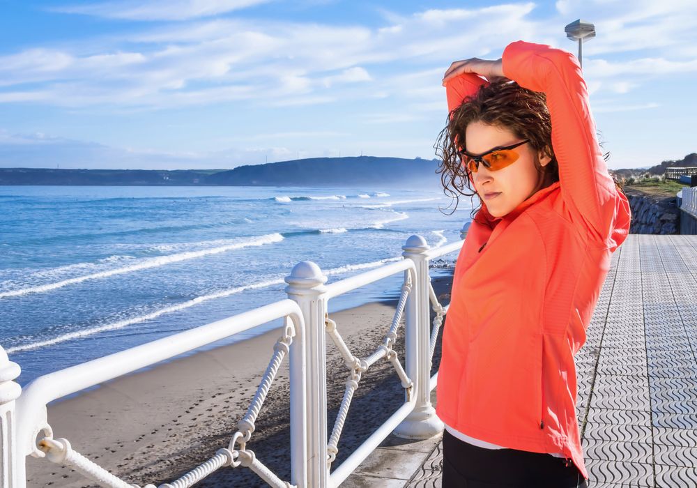 Athletic woman stretching triceps before running on the beach promenade on a summer morning