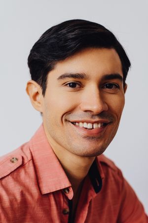 Vertical headshot of smiling Hispanic male in grey studio