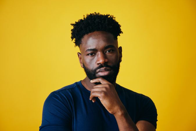 Portrait of calm Black man contemplating with hand to chin on yellow background