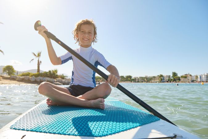 Cheerful kid sitting on SUP board and rowing