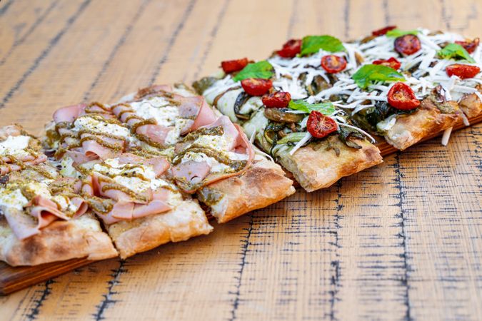 Gourmet Italian Pizza Slices with Ham, Vegetables, and Cheese on Rustic Wooden Board