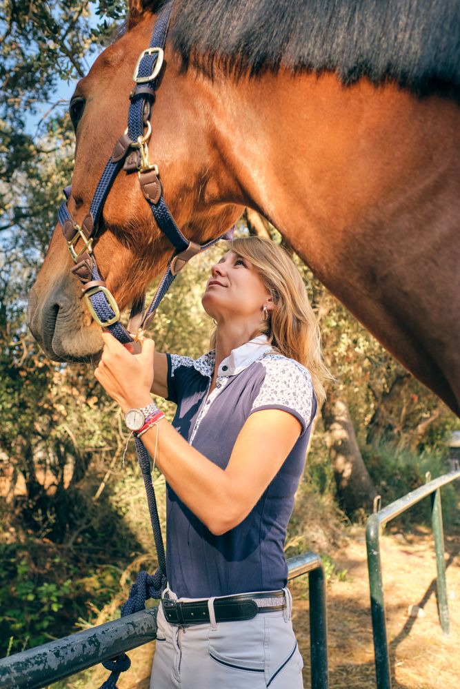 Horsewoman stroking muzzle of horse in paddock