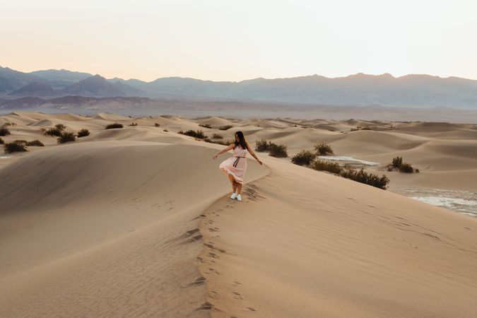 Back view of young woman walking in desert leaving footprints in dry sandy dunes in Death Valley