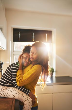 Daughter rests on mother’s chest in bright kitchen