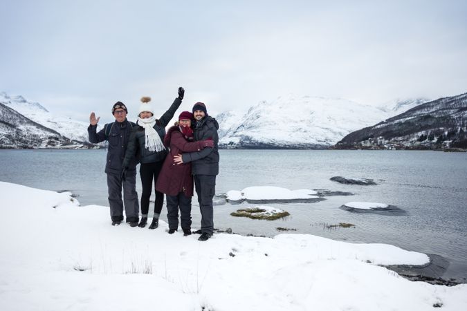 Happy friends on river beach against snowy highland in cold wintry day