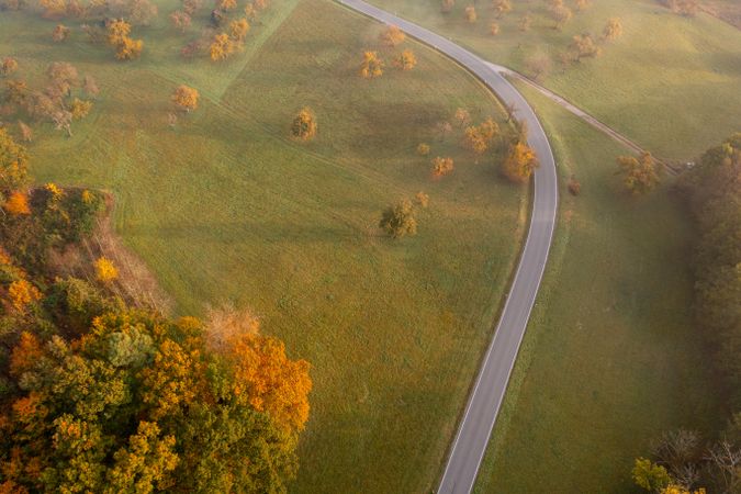 Winding road through autumn nature at sunrise, drone aerial view.