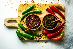Looking down at pot of traditional Georgian sauce Adjika with garlic bulb & raw ingredient on wooden cutting board