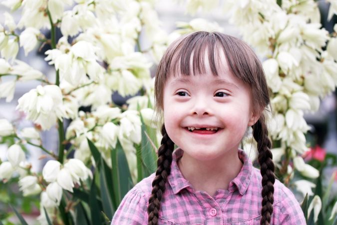 Smiling young girl with Down syndrome outside with spring flowers