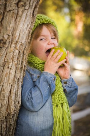 Young Girl Wearing Green Scarf and Hat Eating Apple Outside