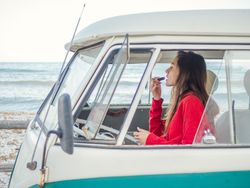 Woman painting lips looking in front mirror of car