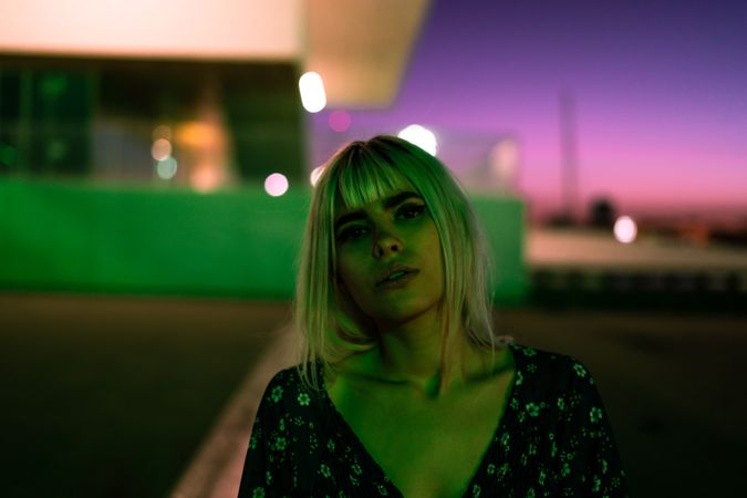 pensive adult woman looking at camera against vibrant sky at dusk