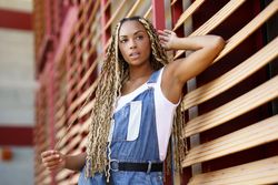 Female in vest and overalls posing on window blinds, low angle