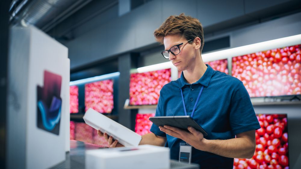 Portrait of a Sales Representative in Home Electronics Store Using Tablet Computer for Online Workflow.