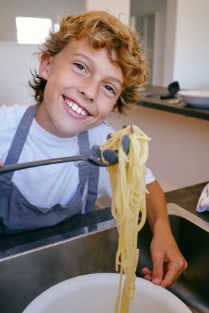 Smiling boy with cooked spaghetti on spatula in kitchen