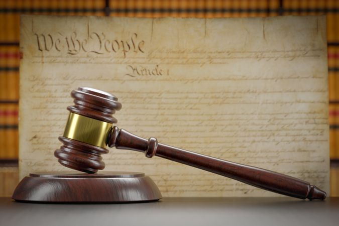 United States Constitution On Wall with Gavel Resting on Table in Front.