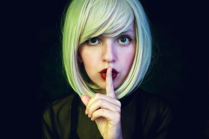 Portrait of woman with blonde short hair and red lipsticks making hush sign