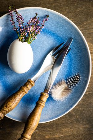 Top view of heather in decorative egg on blue plate with feather