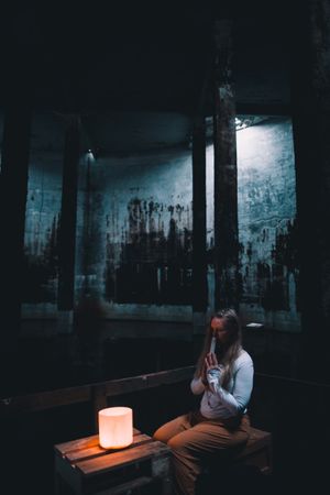 Woman with praying hands near lamp on bench in building