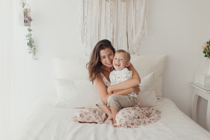 Mother ticking little son and laughing on bed