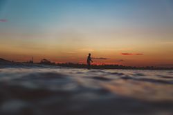 Man with paddle on surf board between waving water at sunset
