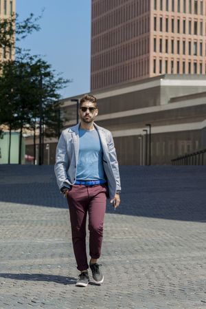Man with sunglasses walking with hand on pocket outside