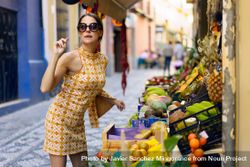 Stylish young woman standing by assorted fruit shop in street 5zr9xk