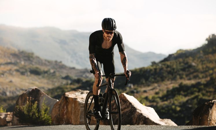Athletic male climbing up the hill on a titanium bicycle