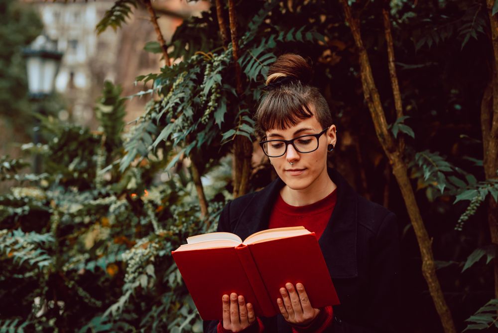 Young woman reading book on bench in park