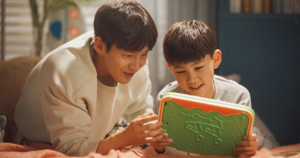 Portrait of Father and Son Playing Video Games on a Digital Tablet at Home.