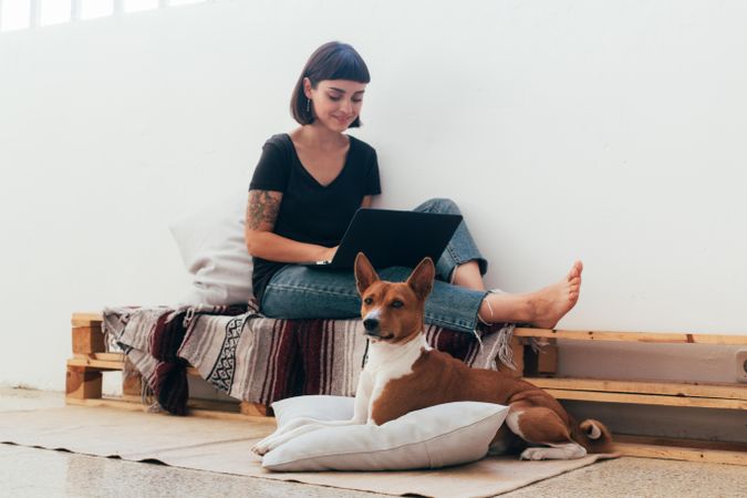 Woman on wooden bench working from home typing on laptop with dog at her feet