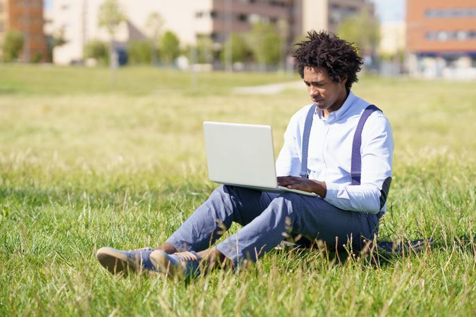 Man in business casual sitting in city part with laptop