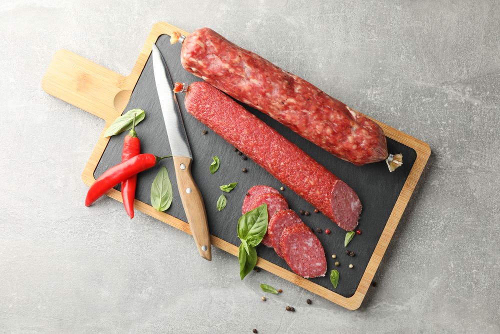 Looking down at two sticks of cured meats with slices on wooden board