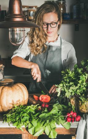 Woman in glasses cutting tomato in rustic kitchen