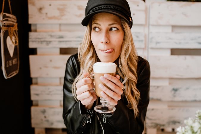 Stylish woman holding coffee in hands and licking lips