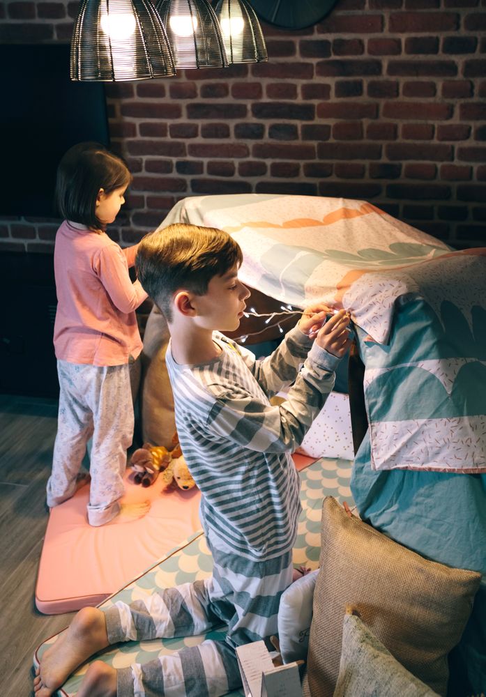Boy helping lsister putting garland of lights in a tent