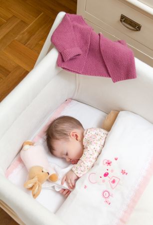 Baby girl sleeping soundly in a cot with pacifier and toy