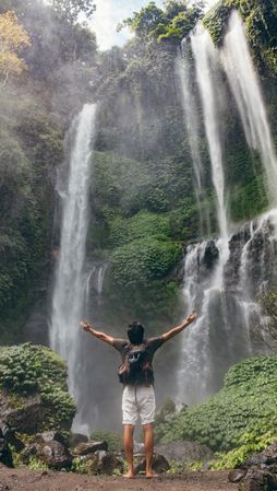 Male tourist with arms outstretched enjoying near waterfall
