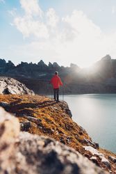 Side view of hiker in red jacket standing on waterside of frozen lake during daytime