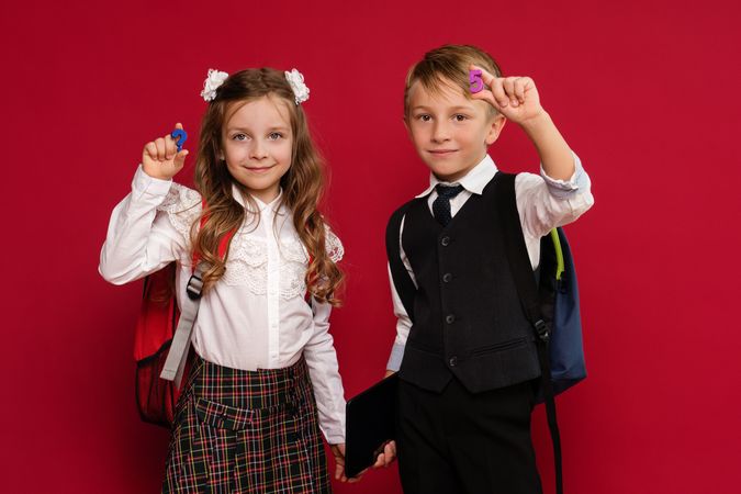 Preteens in school uniform carry backpacks on red background