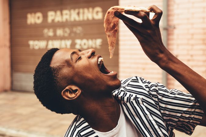 Young man eating pizza slice outdoors