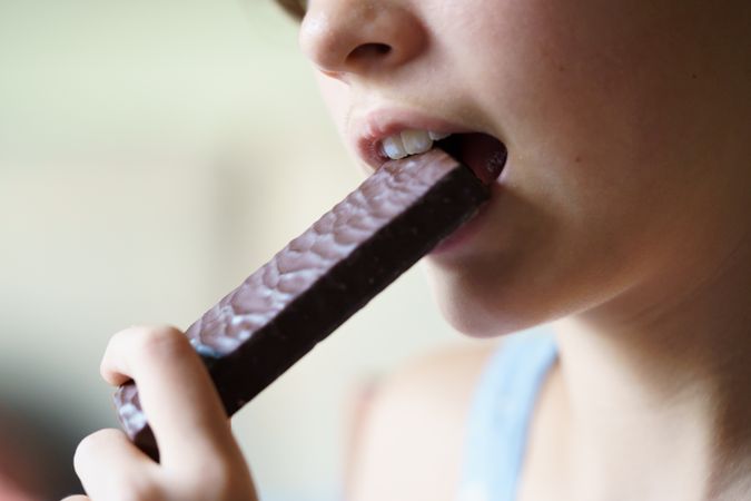 Crop unrecognizable teenage girl eating chocolate bar