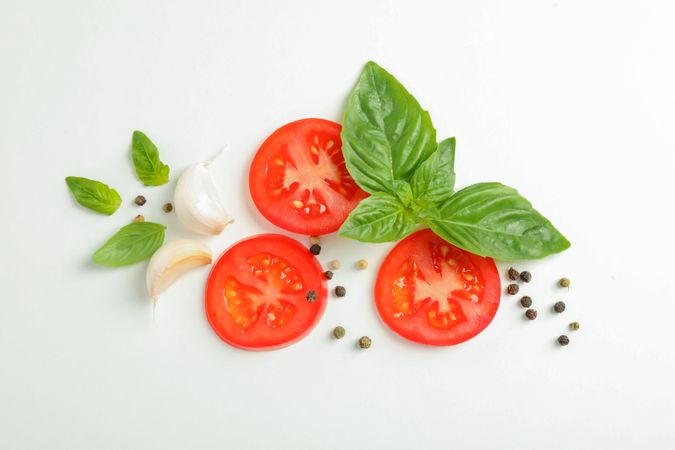 Flat lay composition with fresh cherry tomatoes slices with basil, pepper and garlic on blank background, space for text and top view. Ripe vegetables