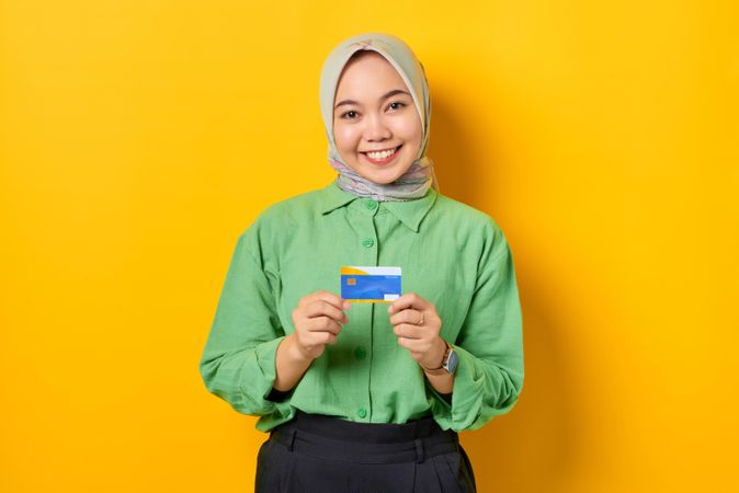 Kind Muslim woman in headscarf and green blouse holding credit card