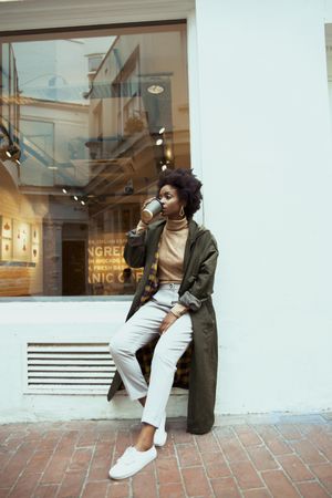 Black woman in green jacket drinking coffee outdoor